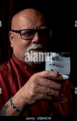 Homme âgé avec l'expression quizzical, comme il se demande si son verre OG bière est à moitié vide ou à moitié plein Banque D'Images