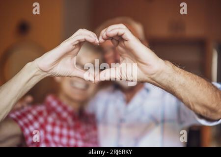 Un couple senior heureux s'embrasse et se forme le cœur avec ses mains. Banque D'Images