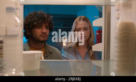 Point de vue POV à l'intérieur du réfrigérateur fille caucasienne femme petite amie femme et homme arabe gars indien petit ami mari multiracial couple la nuit Banque D'Images