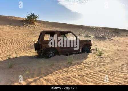 Vue latérale de l'épave de voiture brûlée sur une piste dans le désert entre les dunes, Scorched car Wreck dans le désert Banque D'Images