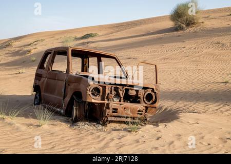 Vue de face de l'épave de voiture brûlée sur une piste dans le désert entre les dunes, Scorched car Wreck Banque D'Images