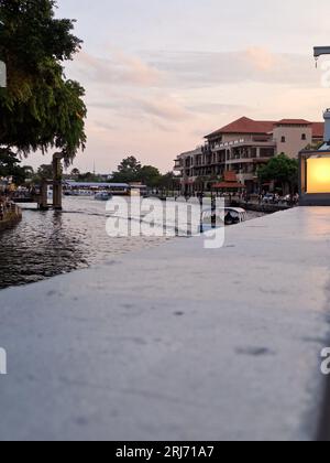 Un petit bateau naviguant sur la pittoresque rivière Melaka en Malaisie, entouré de beaux bâtiments modernes par temps nuageux Banque D'Images