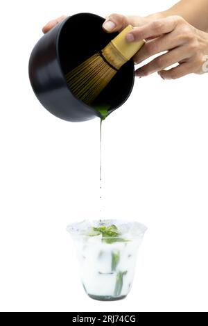 Une main versant du matcha dans une tasse avec de la glace et du lait sur un fond blanc - processus de fabrication du thé matcha Banque D'Images