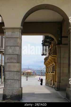 Vue à travers les arches de la Plaza de Maria Pita vers le port avec le paquebot de croisière MSC Virtuosa amarré A Coruña Galicia Espagne Banque D'Images