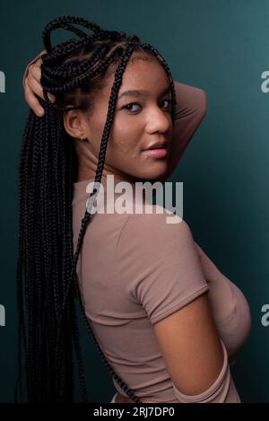 Belle jeune femme aux cheveux tressés, heureuse. Isolé sur fond cyan foncé. Banque D'Images