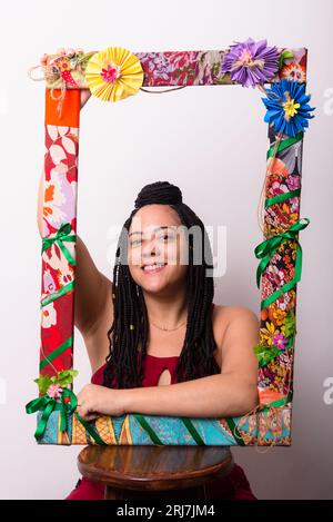 Photo d'une belle femme derrière un cadre orné de fleurs et de tissus colorés en position verticale. Montrant le bonheur sur un backgr de couleur blanche Banque D'Images