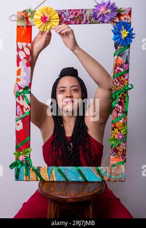 Photo d'une belle femme derrière un cadre orné de fleurs et de tissus colorés en position verticale. Montrant le bonheur sur un backgr de couleur blanche Banque D'Images