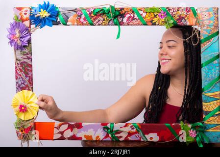 Photo de belle femme avec des tresses dans les cheveux derrière un cadre décoré de fleurs et de tissus colorés dans une position horizontale touchant la fleur Banque D'Images