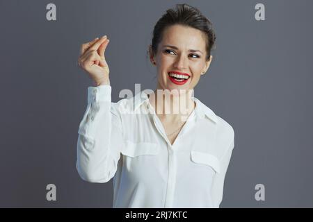 souriant tendance femme d'affaires de 40 ans en blouse blanche doigts claquant isolé sur fond gris. Banque D'Images