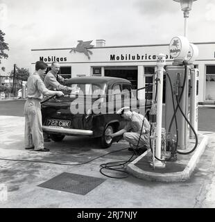 Années 1950, historique, dans une nouvelle station-service Mobilgas, trois préposés en uniforme entretenant une voiture de l'époque, Angleterre, Royaume-Uni ; l'un mettant du carburant, l'autre vérifiant la pression des pneus et l'autre nettoyant le pare-vent arrière. Les années d'après-guerre ont vu une croissance spectaculaire du nombre de propriétaires de voitures et un certain nombre de stations-service ou de stations-service ont été construites pour fournir un service complet, ainsi que des garages et des réparations de voitures. L'époque est devenue connue comme l'âge d'or de l'automobile. Banque D'Images