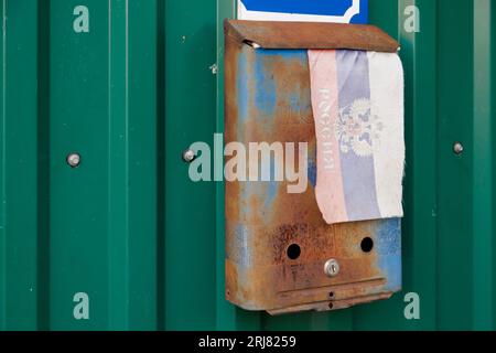 vieille boîte aux lettres russe rouillée sur le mur avec un drapeau russe de petit tissu extrêmement délavé avec armoiries Banque D'Images