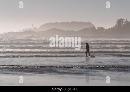 Surfer silhouette in the strong waves on Cox Bay Beach of Tofino with lighthouse in background, Tofino, Vancouver Island, British Columbia, Canada. Stock Photo