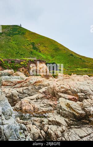 Face de falaise rocheuse de Baren avec des rochers dentelés et une colline montagneuse verte lointaine sous un ciel couvert Banque D'Images