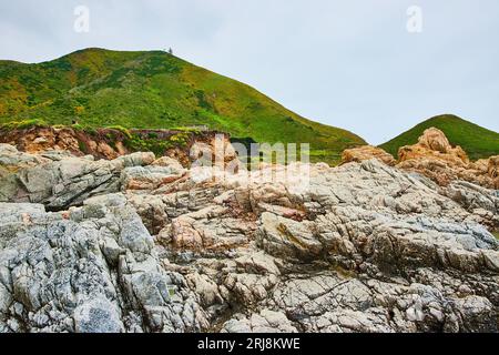 La falaise rocheuse de Baren se dresse dans des rochers déchiquetés avec une colline montagneuse verte lointaine et un ciel couvert Banque D'Images