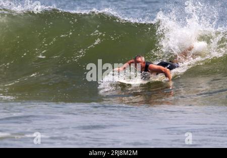 Gilgo Beach, New York, États-Unis - 22 juillet 2023 : un surfeur travaillant dur pour attraper une grande vague au début de sa balade dans l'océan avec un espace de copie sur TH Banque D'Images