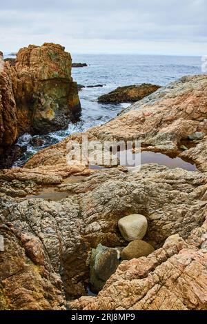 Face de falaise brun foncé rugueuse avec des rochers et des mares de marée tandis que l'océan Pacifique coule entre les rochers Banque D'Images