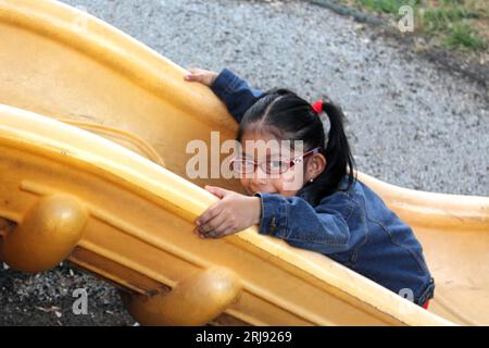 Fille de 4 ans brune Latina joue sur le toboggan dans le parc vivant dans la pauvreté et heureux Banque D'Images