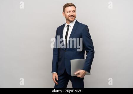Homme d'affaires réussi look confiant avec ordinateur portable à la main debout fond gris isolé. Banque D'Images