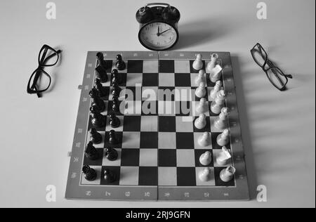 Image en noir et blanc de vieux сhessboard imparfait avec des morceaux. Les verres sont sur les côtés, shabby Dusty réveil montre l'heure. Banque D'Images