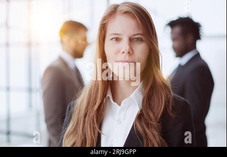 Une belle femme d'affaires se tient debout et regarde avec confiance dans la caméra sur le fond de ses collègues Banque D'Images