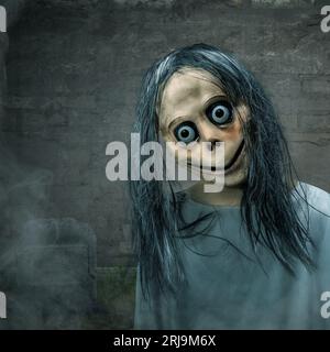 Effrayant Momo debout dans le cimetière avec un fond sombre. Visage effrayant pour Halloween. Concept Halloween Banque D'Images