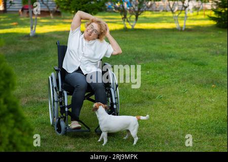 Une femme âgée heureuse en fauteuil roulant se réjouit de marcher avec un chien à l'extérieur. Banque D'Images