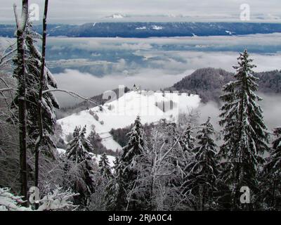 Vue panoramique de l'église de St. Primoz et Felicijan à Jamnik et le brouillard et la brume couvert paysage de Gorenjska, Slovénie derrière en hiver Banque D'Images