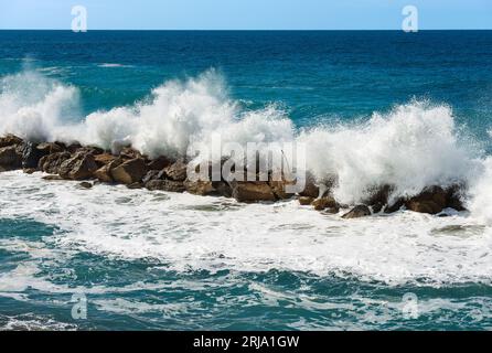 De grandes vagues blanches de la mer se brisent sur les rochers. Brise-lames près du petit village de Framura. La Spezia, Ligurie, Italie, Europe. Mer Méditerranée. Banque D'Images