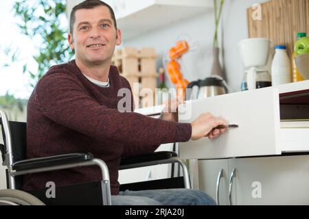 homme handicapé sur fauteuil roulant laver la vaisselle dans la cuisine Banque D'Images