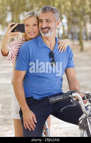 couple heureux avec des vélos prenant selfie dans le parc d'été Banque D'Images