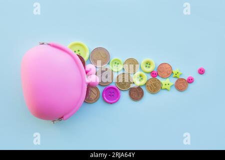 Concept de l'argent des enfants. Pièces et boutons en euros dispersés autour du portefeuille de couleur rose sur fond bleu studio. Espace de copie. Banque D'Images