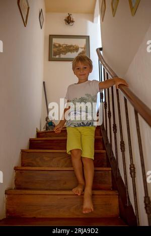 Triste petit enfant en bas âge, garçon, assis triste sur un escalier à la maison, puni, vieille maison autentique Banque D'Images