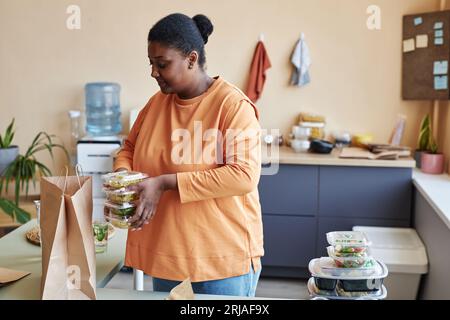 Portrait de femme noire déballant le sac de livraison de nourriture dans la cuisine et souriant, espace de copie Banque D'Images