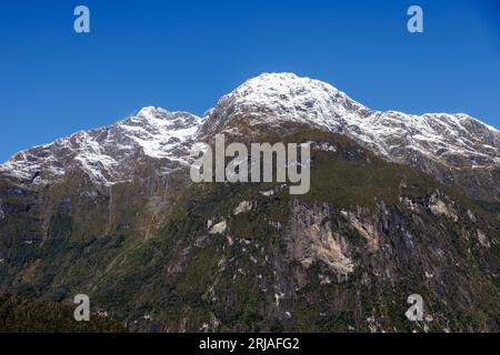 Une chaîne de montagnes enneigées avec de la végétation verte et plusieurs cascades. Cette gamme se trouve dans les Milford Sounds, en Nouvelle-Zélande Banque D'Images