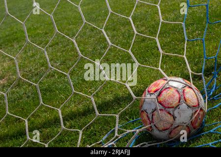 vieux ballon de football dans le filet sur le fond du terrain de football de l'herbe. Jour ensoleillé d'été. Banque D'Images