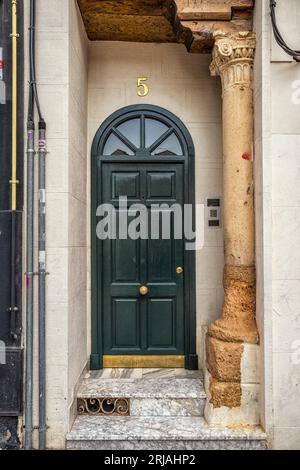 Dark green door in the city of Guadalajara, Spain. Arched Georgian door house and an old antique column in the doorway. Facade with cables and pipes. Banque D'Images