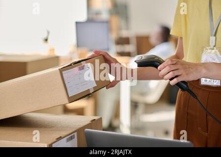 Gros plan d'une jeune femme scannant des codes qr sur des boîtes emballées avec des marchandises commandées en ligne tout en se tenant devant la caméra dans l'entrepôt Banque D'Images