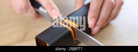 Femme aiguisez le couteau avec un taille-crayon sur la table de cuisine en gros plan. Banque D'Images