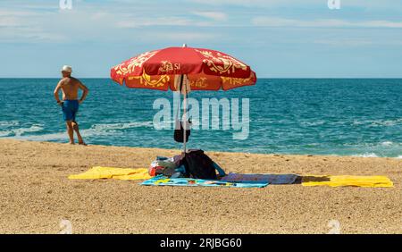 L'homme se tient près de la mer près d'un parasol abritant des affaires, Nazare, Portugal Banque D'Images