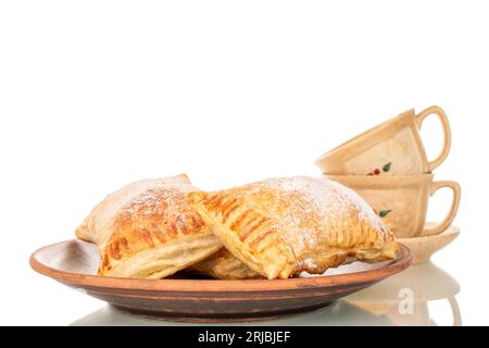 Trois pains feuilletés aromatiques avec des pommes sur une assiette d'argile avec deux tasses, macro, isolé sur fond blanc. Banque D'Images