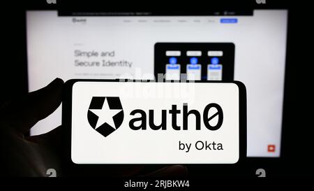 Personne détenant un smartphone avec le logo de la société de plate-forme d'identité américaine Auth0 by Okta sur l'écran en face du site Web. Concentrez-vous sur l'affichage du téléphone. Banque D'Images