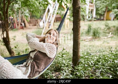 joyeuse jeune femme blonde dans les vêtements boho se relaxant dans hamac dans le centre de retraite Banque D'Images