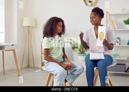 Professeur psychologue afro-américain montre carte avec émoticône souriant à la fille. Banque D'Images