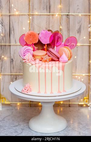 Gâteau blanc avec chocolat fondu rose, meringues et sucettes sur fond festif Banque D'Images