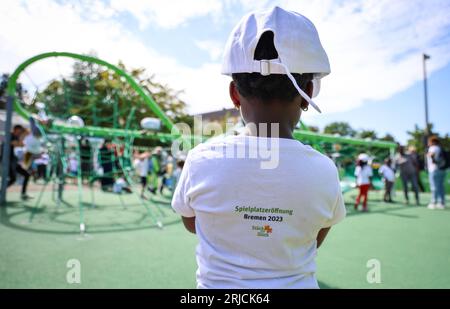 Brême, Allemagne. 22 août 2023. Une jeune fille portant un T-shirt avec l'inscription "Playground Opening in Bremen 2023" se tient devant un équipement de terrain de jeu à l'ouverture de la première aire de jeux inclusive à Brême à la garderie de la congrégation de l'église Dietrich Bonhoeffer. L'aire de jeux offre également un accès sans obstacle à divers équipements de jeux pour les enfants handicapés. Crédit : Focke Strangmann/dpa/Alamy Live News Banque D'Images