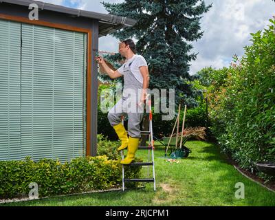 Taille professionnelle du jardinier. Tondre la pelouse. Jardinier masculin, portant dans des combinaisons avec des gants de protection travaillant avec du matériel de jardin professionnel. Banque D'Images