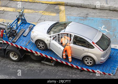 Voiture endommagée chargée sur une dépanneuse par un travailleur. Service de remorquage sur la ville. Concept d'assistance routière Banque D'Images