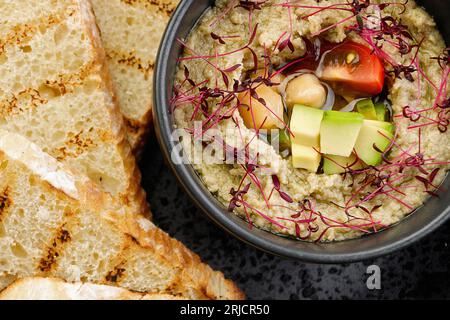 Houmous à l'avocat et aux tomates sur une assiette noire avec toasts de pain, sur fond de bois Banque D'Images