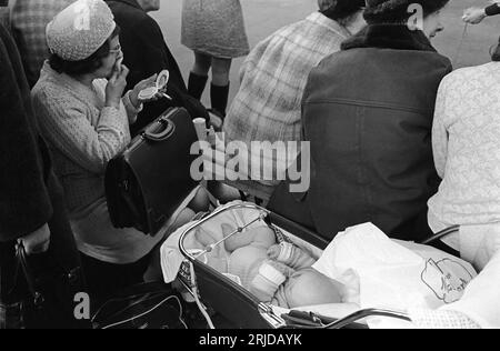 Années 1960 Earls court, Londres, Crufts Dog Show au parc des expositions Olympia. Une femme d'âge moyen mettant sur son maquillage à l'aide d'un paquet de poudre, avec son bébé dans une poussette dans la foule regardant les chiens être jugés. Earls court, Londres, Angleterre février 1968. HOMER SYKES. Banque D'Images