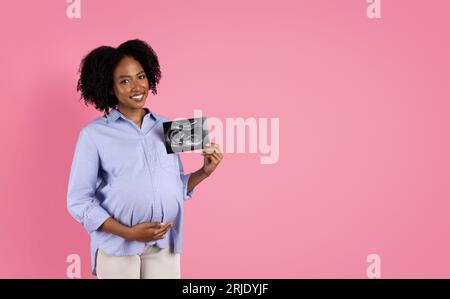 Joyeuse jeune femme enceinte noire dans le ventre touchant occasionnel, montrer l'échographie Banque D'Images